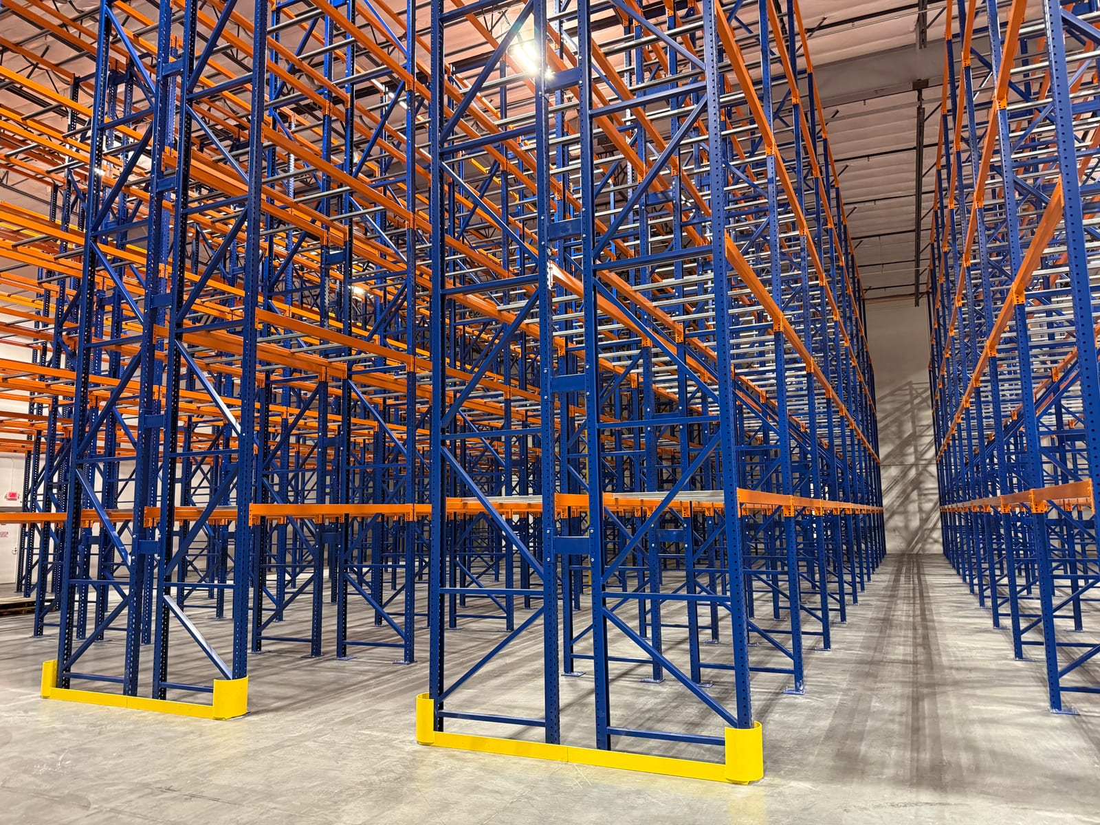 Rows of tall blue and orange selective pallet racking with yellow end-of-aisle guards in a temperature-controlled warehouse